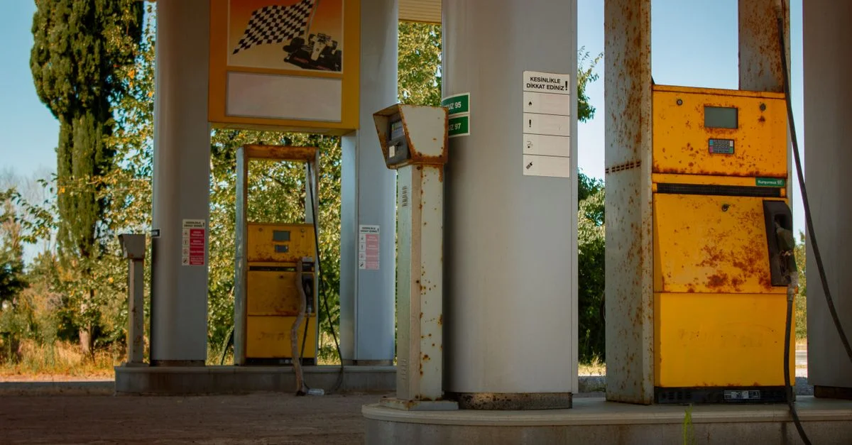 Vue extérieure d'une station-service abandonnée avec des pompes rouillées et une végétation envahissante.