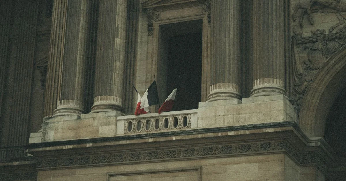 Gros plan d'un bâtiment historique avec des drapeaux français et de grands colonnes, mettant en valeur une architecture ornée.