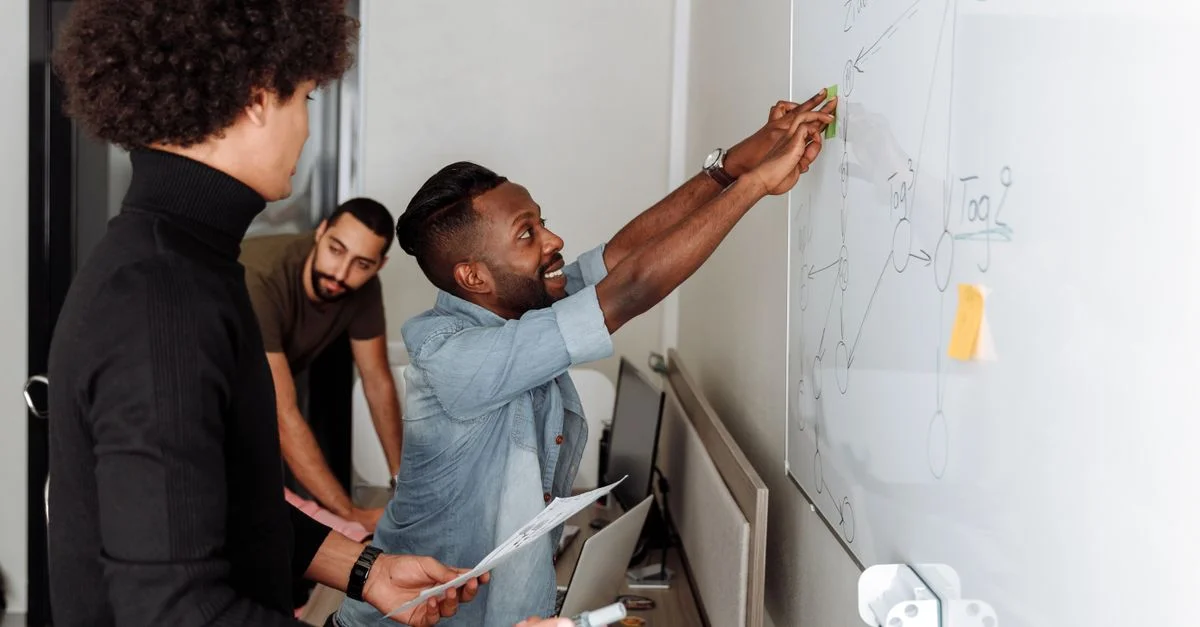 Une équipe diversifiée de professionnels en train de réfléchir à des solutions devant un tableau blanc dans un cadre de bureau.