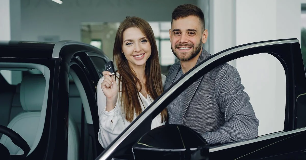 Un couple joyeux dans un showroom de voitures tenant des clés de voiture, symbolisant un nouvel achat.