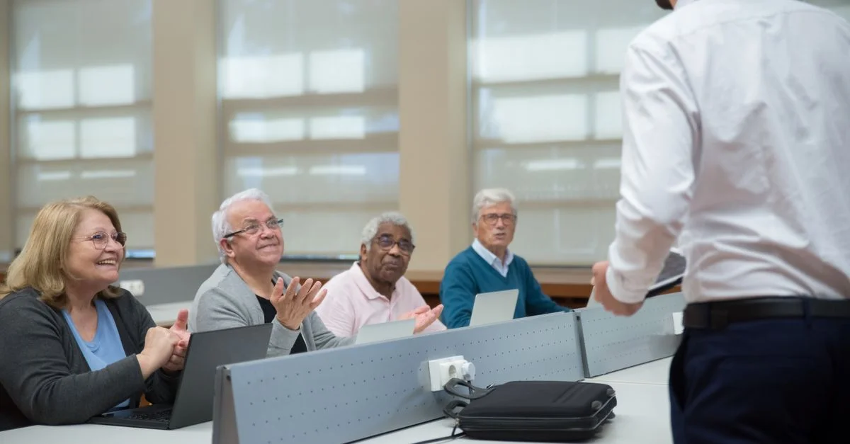 Des adultes seniors assistent à un cours d'informatique, dirigé par un instructeur, dans une salle de classe.