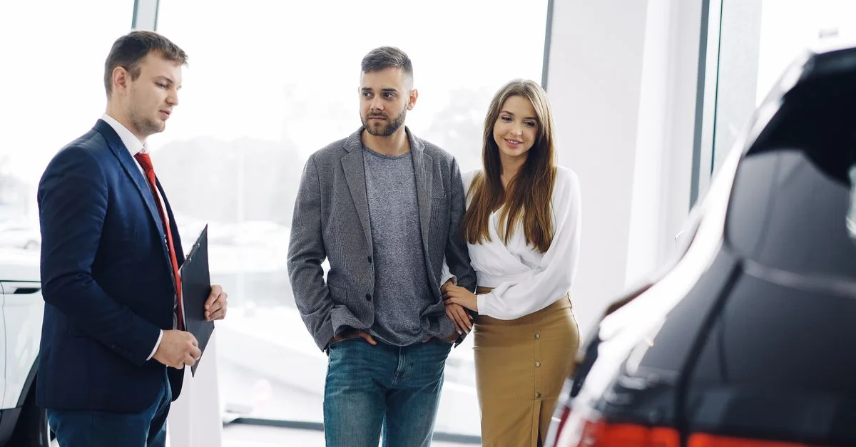 Un couple souriant discute des caractéristiques d'une voiture avec un vendeur dans une salle d'exposition automobile.