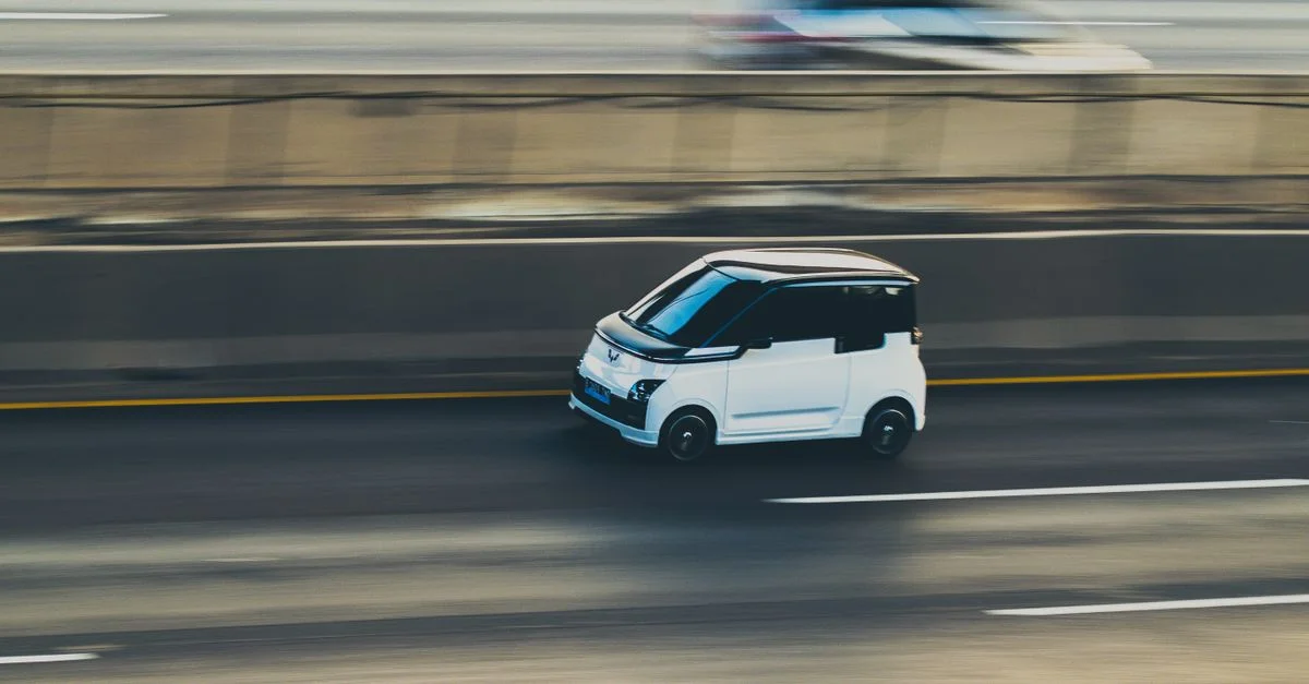 Une voiture électrique compacte blanche est filmée en mouvement sur une autoroute grâce à une technique de panoramique dynamique.