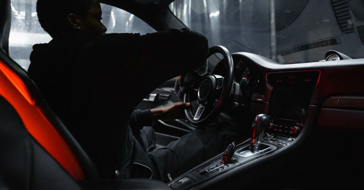 Un homme afro-américain nettoyant l'intérieur d'une voiture de luxe avec un focus sur le volant et le tableau de bord.