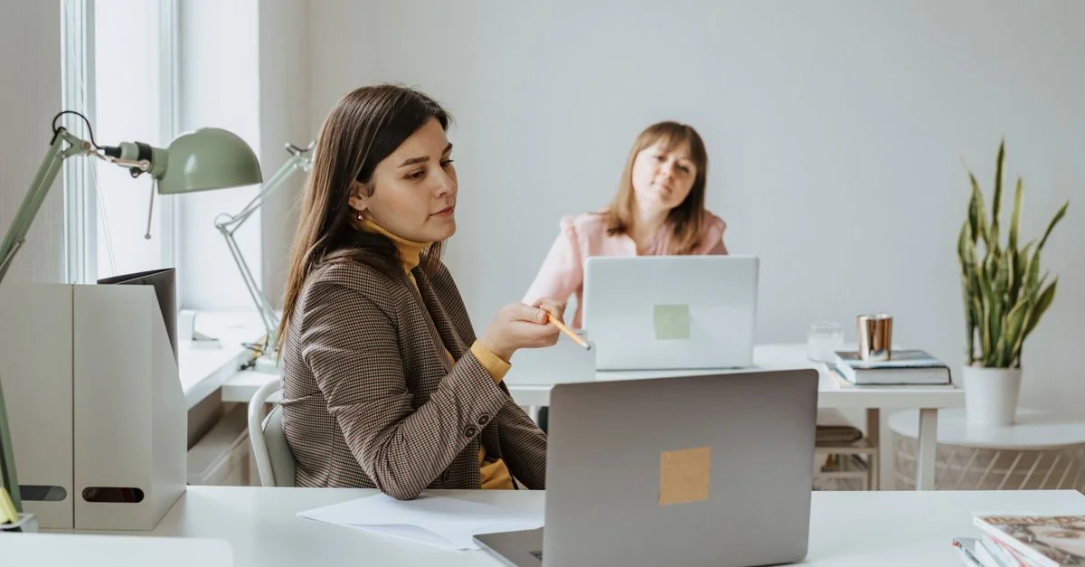 Deux femmes travaillant ensemble dans un cadre de bureau moderne, utilisant des ordinateurs portables et discutant d'idées.