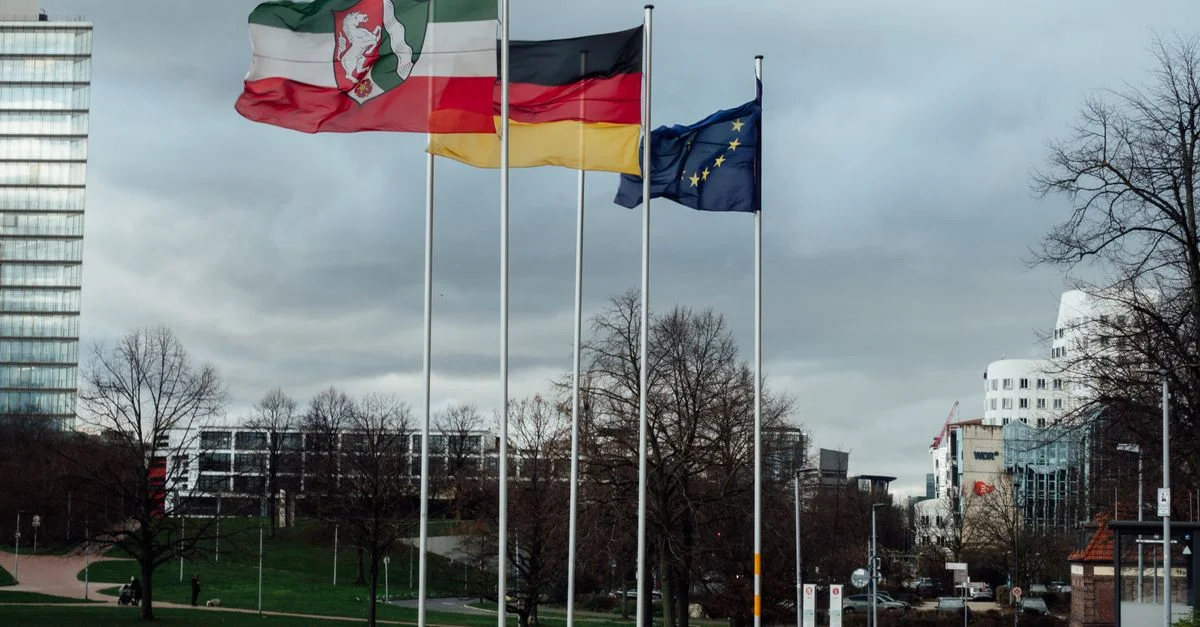 Drapeaux européens et nationaux dans un espace public de Düsseldorf, mettant en valeur l'architecture moderne.